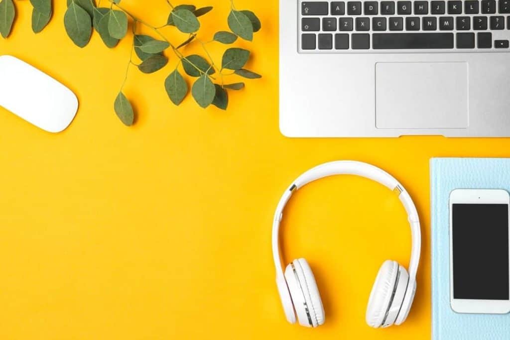 Still life of a woman's home office with a laptop, headphones, and phone.