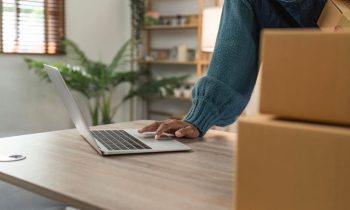 An Etsy seller using a laptop while preparing products for shipment.