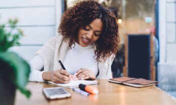 A remote nonprofit worker working at an outdoor table and writing in a notebook.