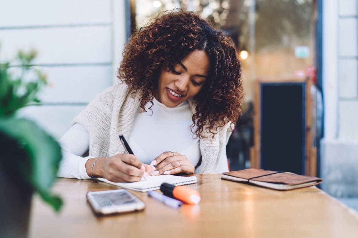 A remote nonprofit worker working at an outdoor table and writing in a notebook.