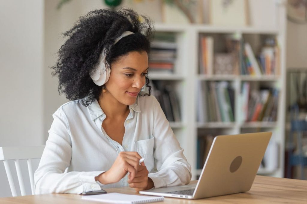 A teacher working from her home office on a laptop with books in the background.