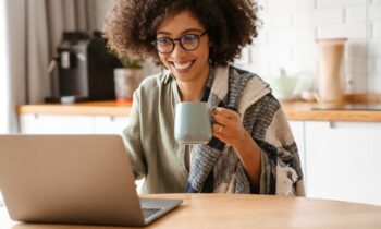 A woman working from home and drinking coffee at her computer.