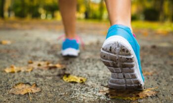 A closeup of a woman's running shoes, running on pavement outdoors.