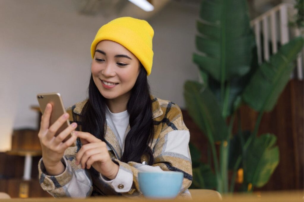 A young woman looking at social media on her phone in a coffee shop.