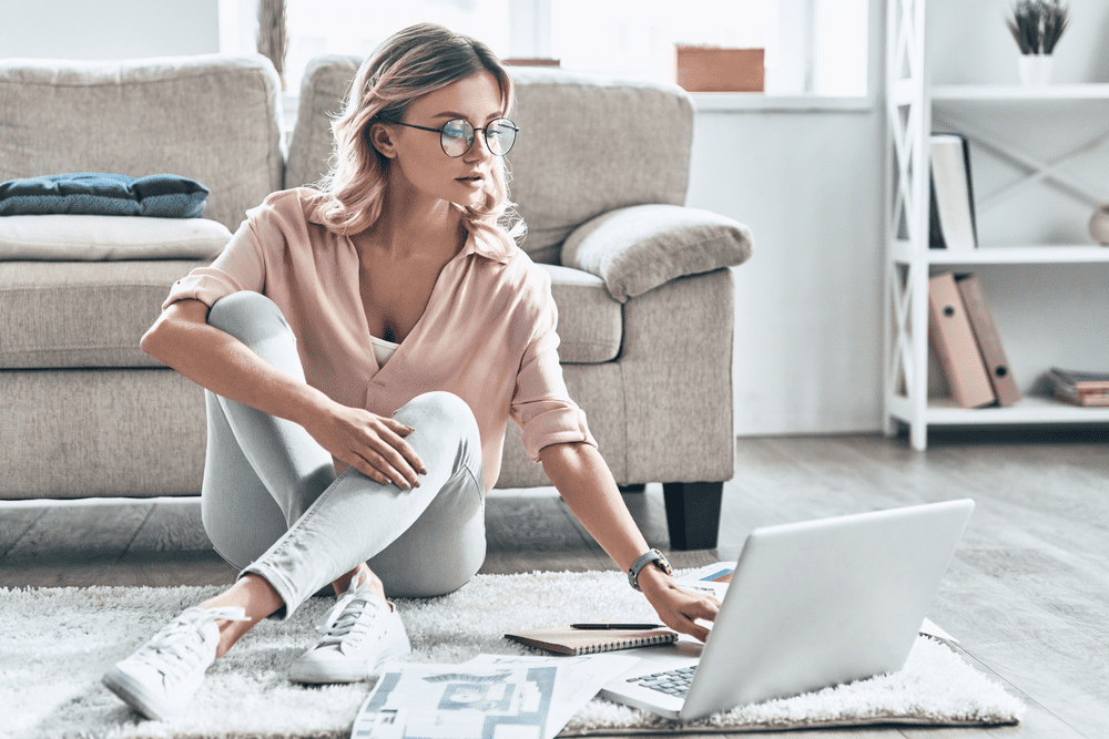 Young woman dressed casually sitting on ground working on laptop