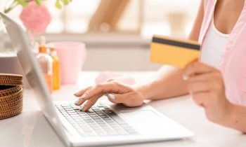 A closeup image of a woman sitting at a desk, shopping online, using a coupon site, and holding a credit card.