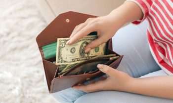 A woman, holding a wallet and putting a $5 bill into it.