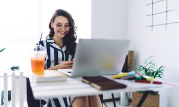 A remote freelancer is working from her home office at a desk, using a laptop and a smart phone.