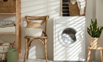 A laundry room in someone's home, with a washing machine, chair, and basket of clothes.