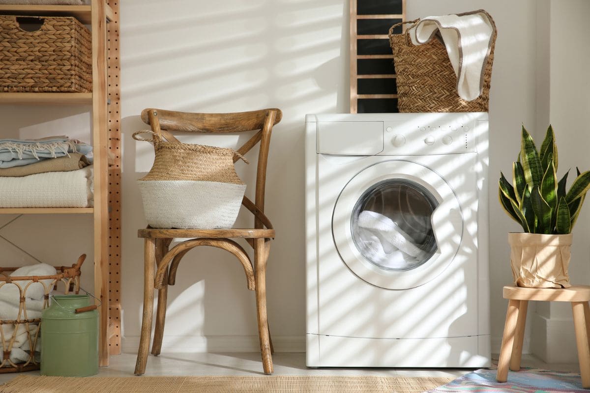 A laundry room in someone's home, with a washing machine, chair, and basket of clothes.