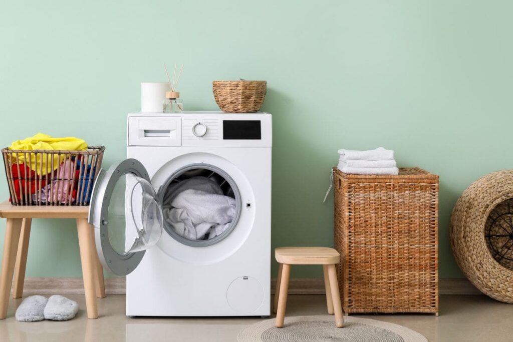 A laundry room in someone's home, with a washing machine, hamper, and a basket of clothes.