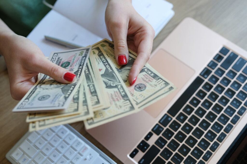 A woman sitting at her home office desk, counting cash while working on a budget.