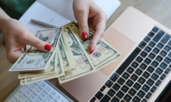 A woman sitting at her home office desk, counting cash while working on a budget.