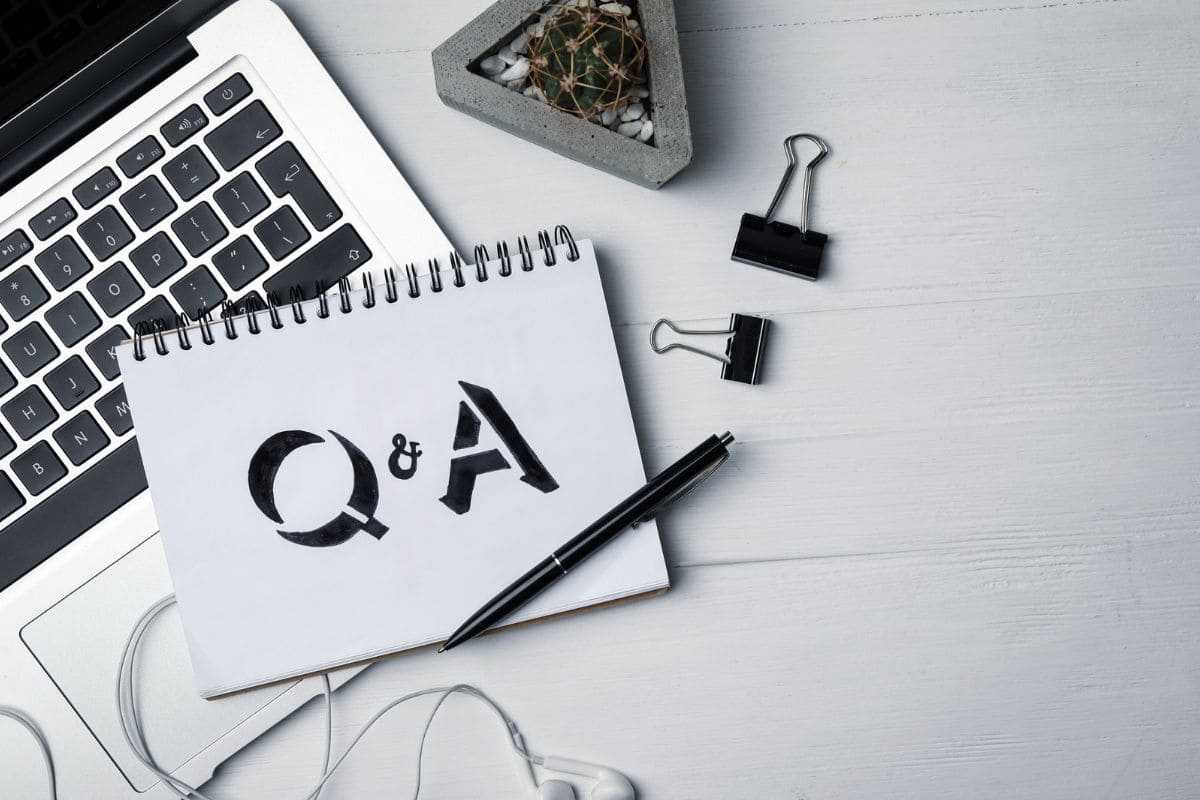 A desk with a laptop, ear phones, a cactus, and a notebook with "Q&A" written in it.