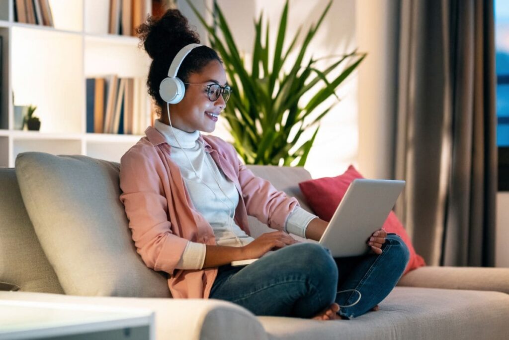 A woman working from home on her couch, using a laptop and headphones.