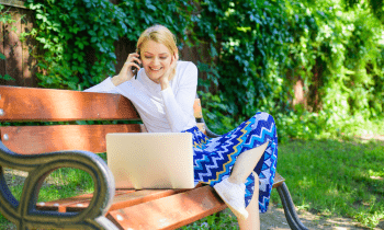 Working sitting on a park bench working on her laptop talking on the phone