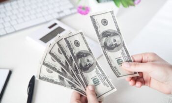 A woman counting cash at her computer desk for blog post: How to Make 10K a Month