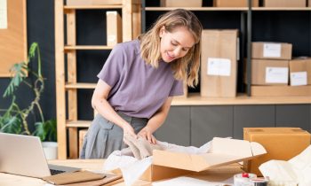 A woman in her home office, packing products into shipping boxes.