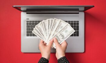 A woman's hands holding cash next to a laptop.