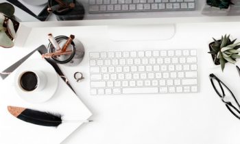 cup of coffee sitting next to a computer, plant, and eye glasses