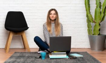 A woman sitting on her living room floor, using a laptop to take paid surveys online.