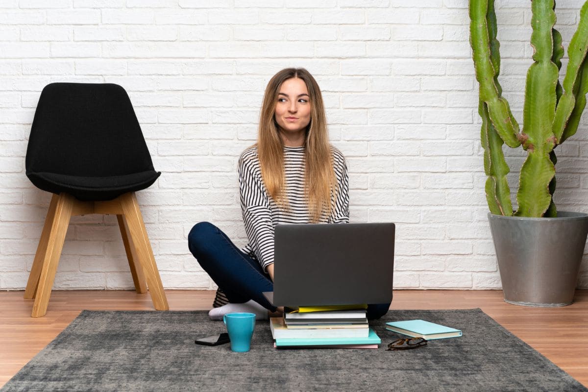 A woman sitting on her living room floor, using a laptop to take paid surveys online.