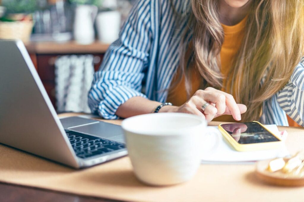 A woman sitting at her home office desk, using a laptop and phone.