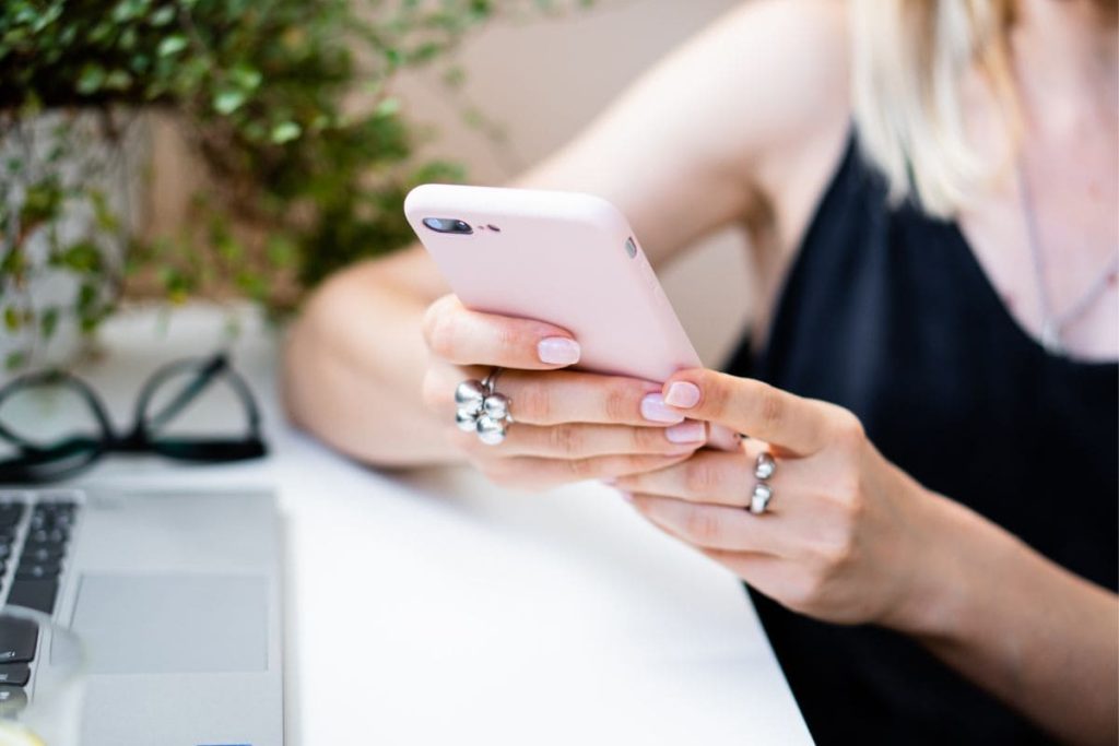 Closeup image of a woman using a smartphone while sitting at her home office desk.