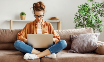 woman wearing glasses sitting cross-legged on sofa working on her laptop to make extra money online