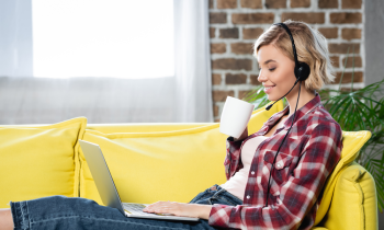 Young female tech support agent sitting on sofa working on laptop