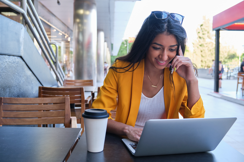 Young woman working at a cafe on her laptop for her flexible work from home jobs